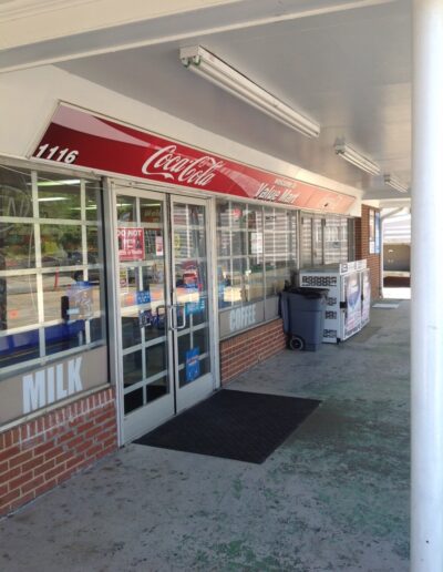 Convenience store entrance with Coca-Cola signage, windows displaying various products and milk.